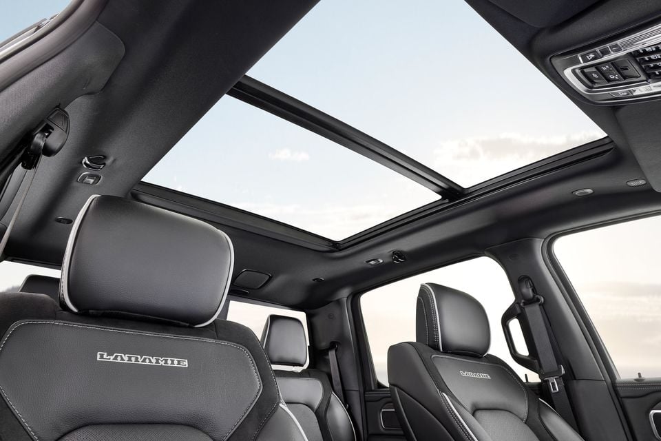 Interior of a Ram 1500 Laramie showing dark leather seats with Laramie embroidery and a large panoramic sunroof open to a cloudy sky