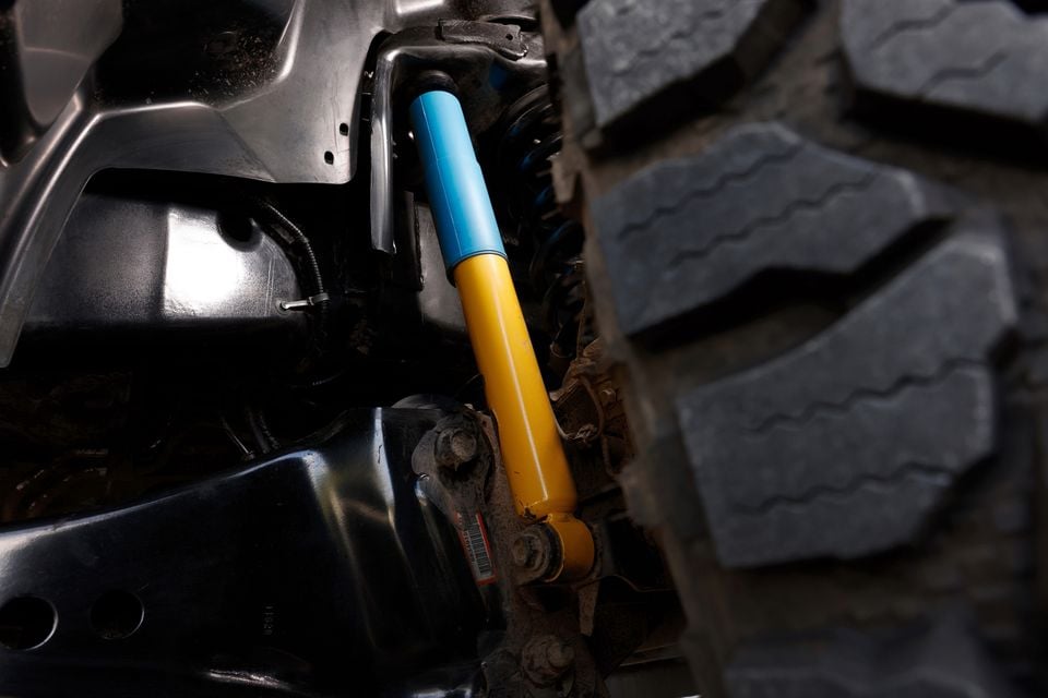 Close-up of a blue and yellow Bilstein shock absorber and suspension components on a Ram 2500 Warlock, with a large off-road tyre visible alongside