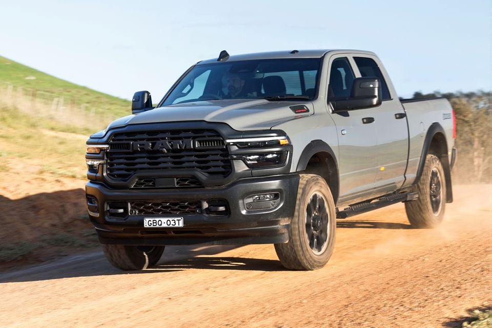 A silver 2026 Ram 2500 Warlock pickup truck driving on a dirt road, seen from the front quarter view.