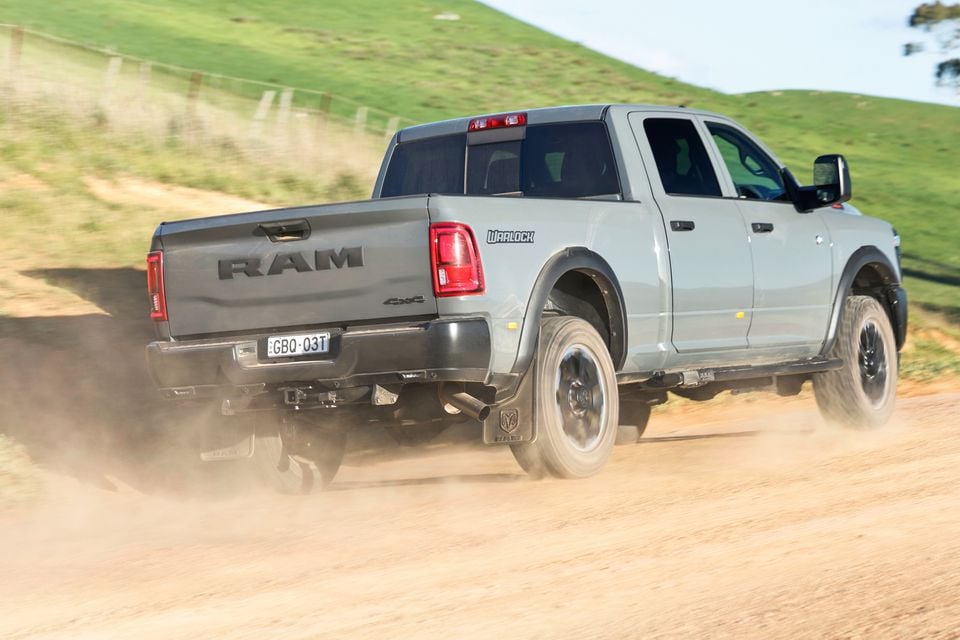 A grey Ram 2500 Warlock 4x4 pickup truck driving on a dirt road, kicking up dust, seen from the rear