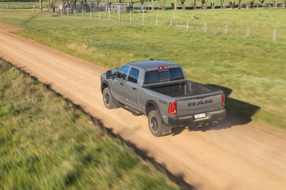 A grey Ram 2500 Warlock ute drives along a dirt farm road, seen from an elevated rear angle
