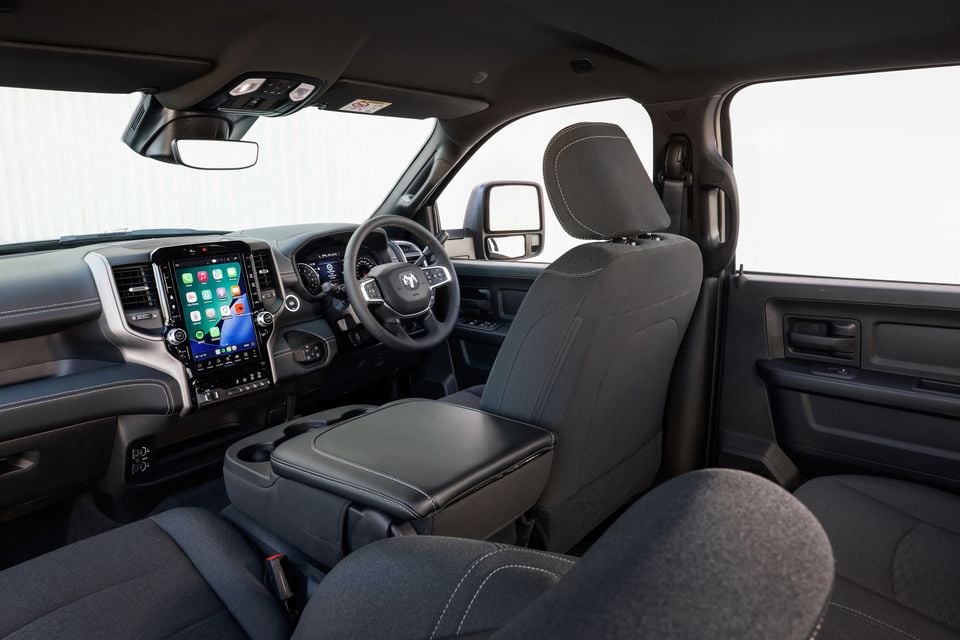 Interior of a Ram 2500 Warlock ute showing the front cabin with dark fabric seats, large vertical touchscreen infotainment system displaying Apple CarPlay, and the Ram-branded steering wheel, viewed from the rear passenger side