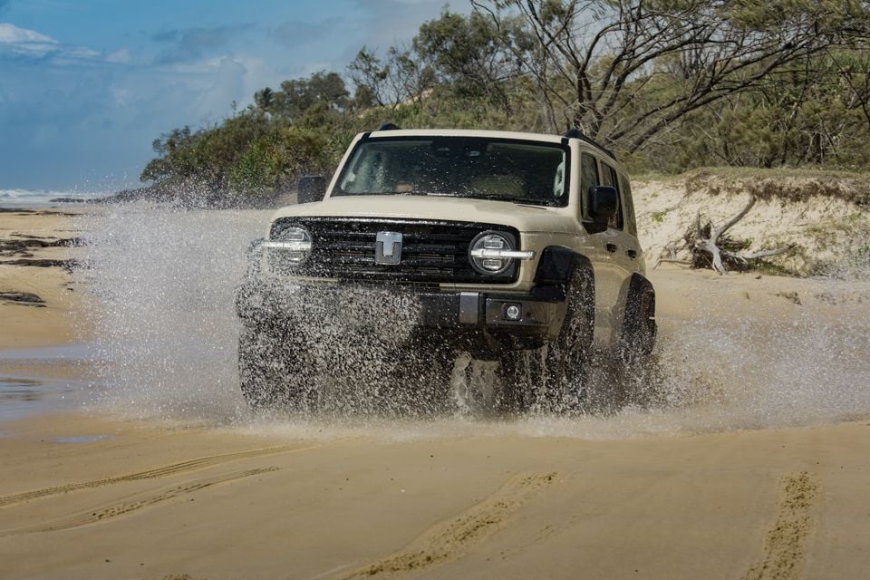 A beige GWM Tank 300 PHEV 4WD SUV driving through water on a sandy beach, seen from the front