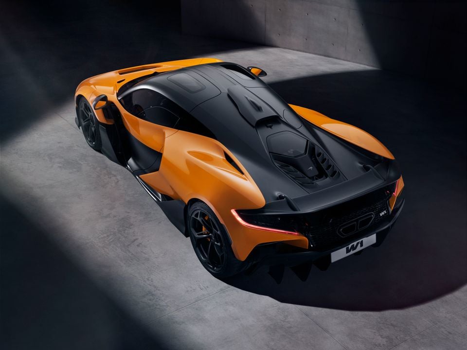 A McLaren W1 supercar in orange and black, seen from a high rear-three-quarter angle in a studio setting