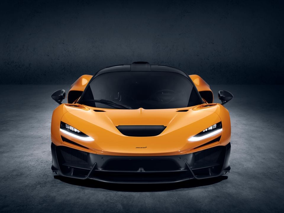 An orange McLaren W1 supercar seen from the front, photographed in a studio setting with dramatic lighting