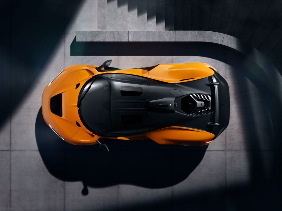 An orange McLaren W1 supercar seen from directly above, revealing its dramatic aerodynamic bodywork and central cockpit design on a concrete surface.