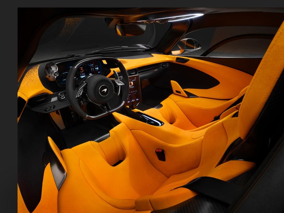 McLaren W1 interior showing vibrant orange bucket seats, carbon fibre trim, McLaren-branded steering wheel, digital instrument cluster and central touchscreen infotainment display