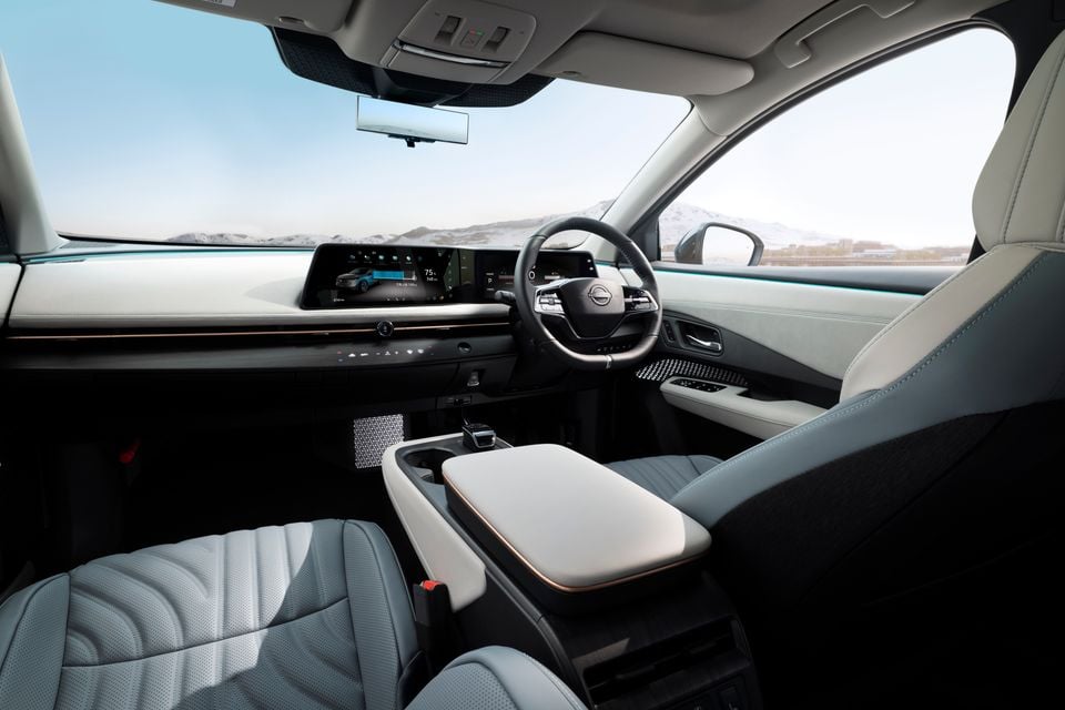 The interior of a Nissan Ariya showing the steering wheel, dual screens and front seats with a view of snowy mountains outside.