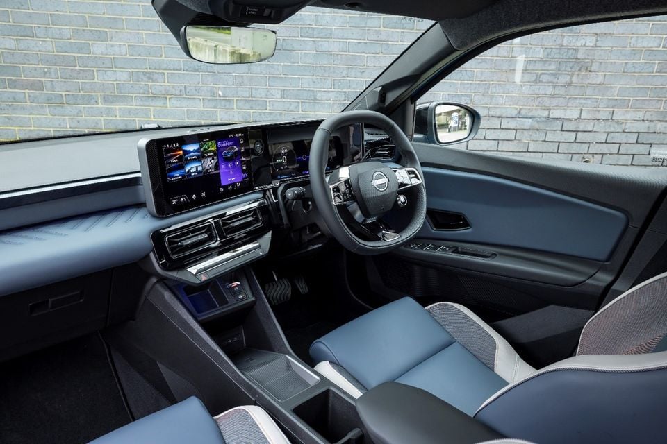 The interior of a Nissan Micra showing the steering wheel, digital dashboard and infotainment screen, with blue and grey leather seats.
