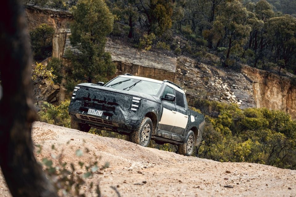 A camouflaged Nissan Navara Pro PHEV prototype dual-cab ute driving along a rocky dirt track in Australian bushland
