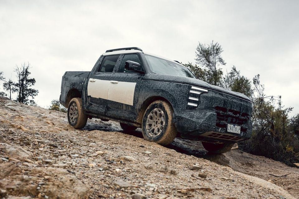 A camouflaged Nissan Navara Pro dual-cab ute prototype driving down a rocky, muddy off-road track