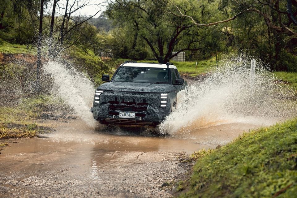 A camouflaged Nissan Navara Pro prototype ute splashing through a muddy water crossing on a bush track