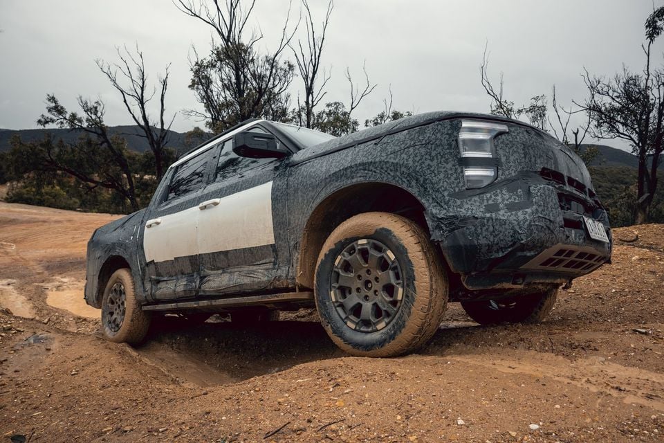 A camouflaged Nissan Navara Pro prototype dual-cab ute seen from the front quarter on a muddy off-road dirt track