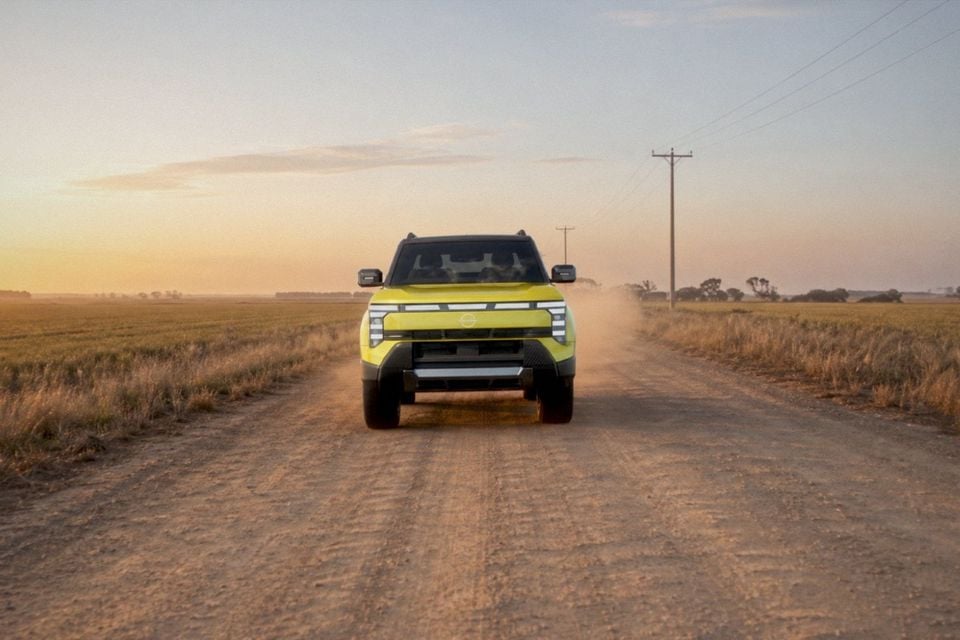 A yellow Nissan Navara Pro seen from the front, driving along a dusty gravel road through farmland at sunset