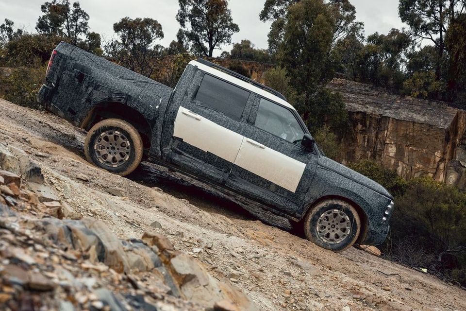 A camouflaged Nissan Navara Pro prototype dual-cab ute driving down a steep rocky off-road track, seen from the side