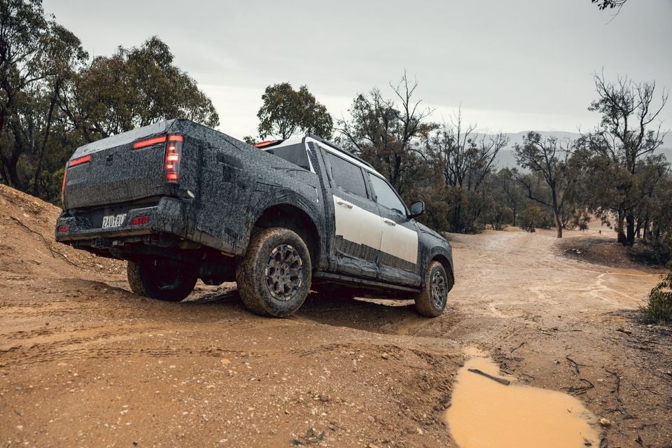 Camouflaged Nissan Navara Pro prototype dual-cab ute climbing a muddy bush track, seen from the rear quarter