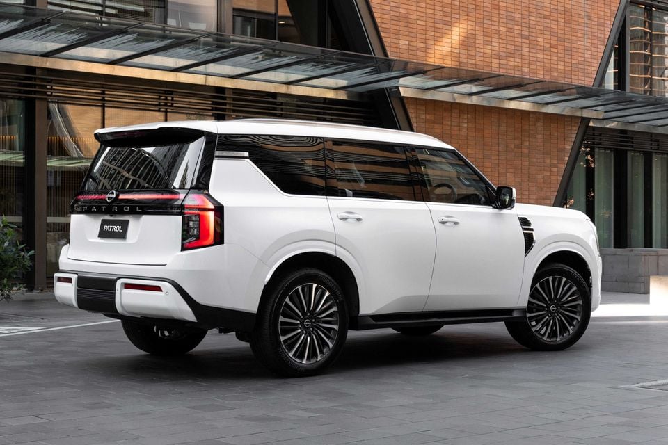 White Nissan Patrol Y63 large SUV seen from the rear three-quarter angle outside a modern building