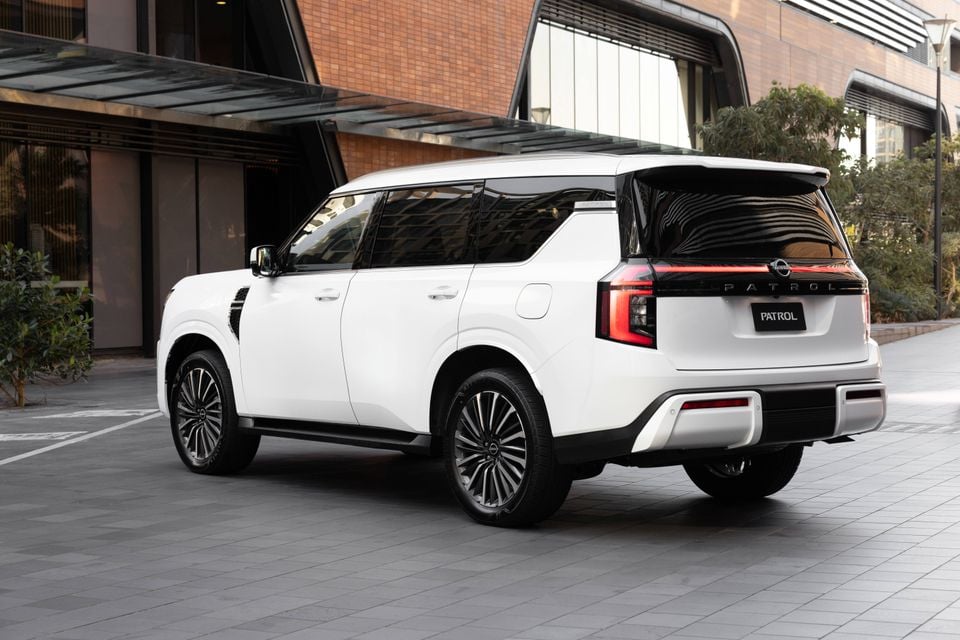 A white Nissan Patrol Y63 large SUV seen from the rear three-quarter angle, parked outside a modern building