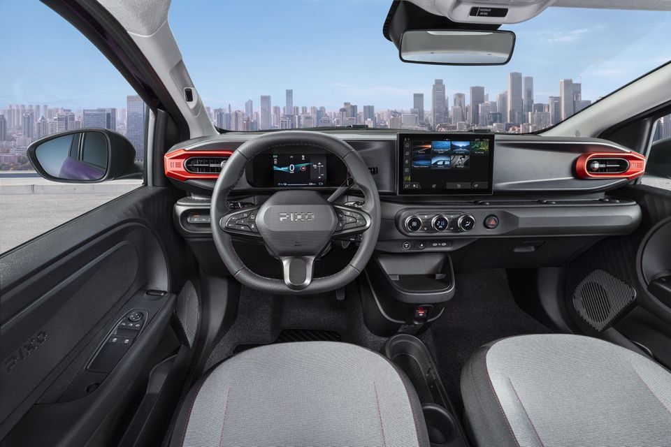 The interior of a Nissan Pixo hatchback, showing the steering wheel, digital instrument cluster, touchscreen and dashboard with a city skyline visible through the windscreen.
