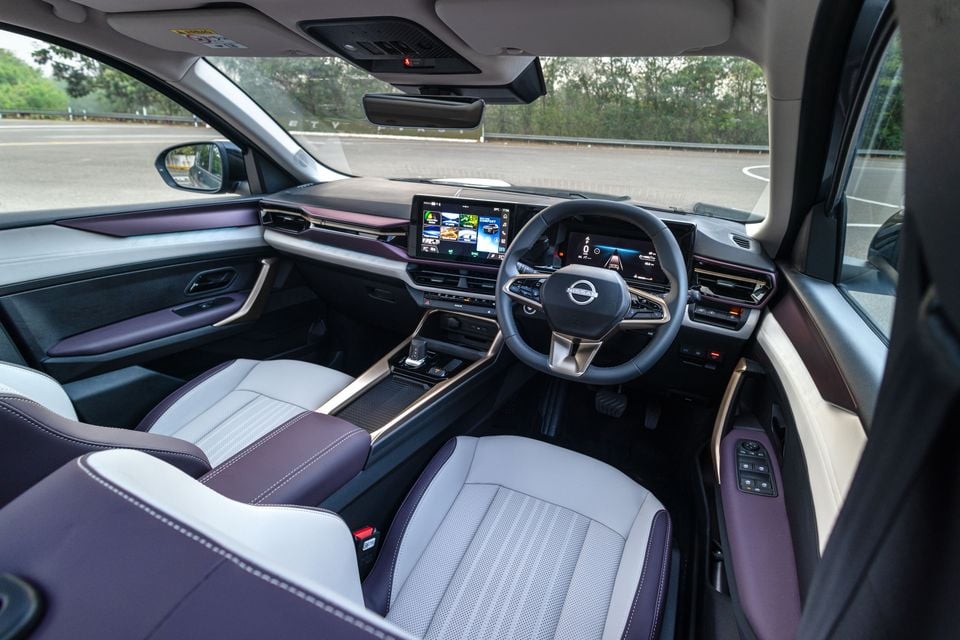 Nissan Tekna interior showing the dashboard, dual screens, two-tone purple and grey leather seats, steering wheel, and centre console viewed from the passenger side door