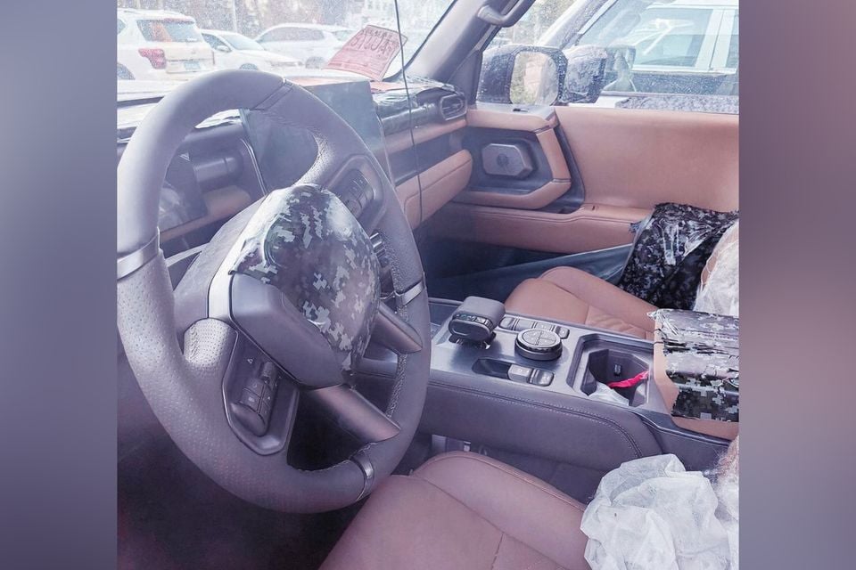 Interior spy photo of an unreleased Nissan Terrano prototype, showing the steering wheel with camouflage covering, tan leather seats, centre console, and partially concealed infotainment screen.