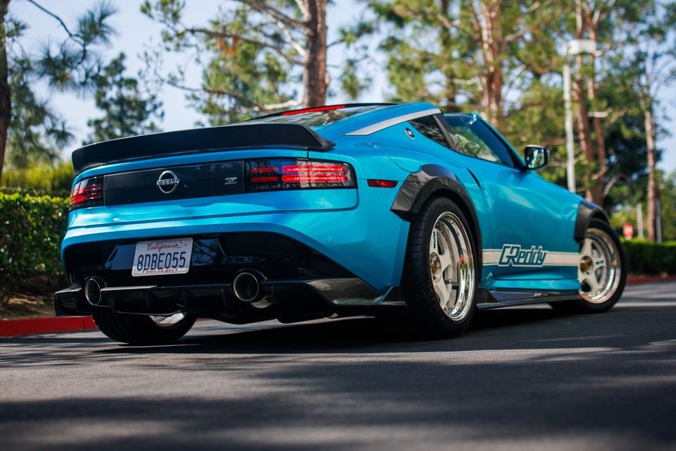 A blue Nissan Z Kaze concept car with a widebody kit and chrome wheels, seen from the rear quarter angle on a road