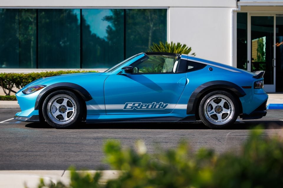 A blue Nissan Z Kaze concept sports car with wide fenders and GReddy livery, seen from the side in a parking lot