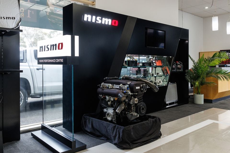 A Nissan NISMO engine on display inside a Nismo Performance Centre showroom, with the Nismo logo illuminated above it
