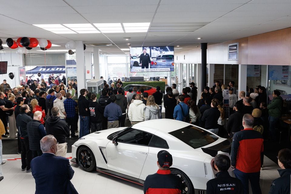 A white Nissan GT-R Nismo sports car on display inside a crowded Nissan dealership showroom during a launch event