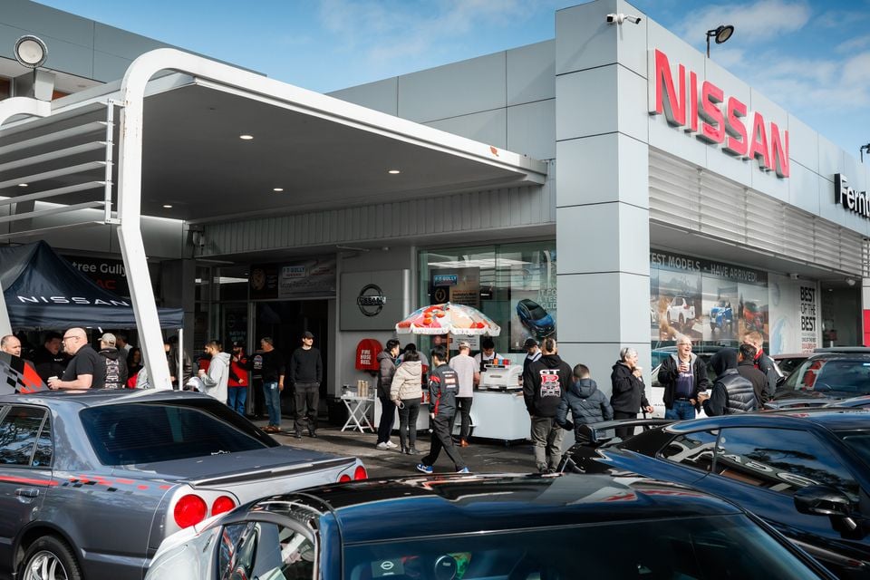 A crowd gathers outside a Nissan dealership with Nissan GT-R and Skyline cars parked in front during a performance centre event.