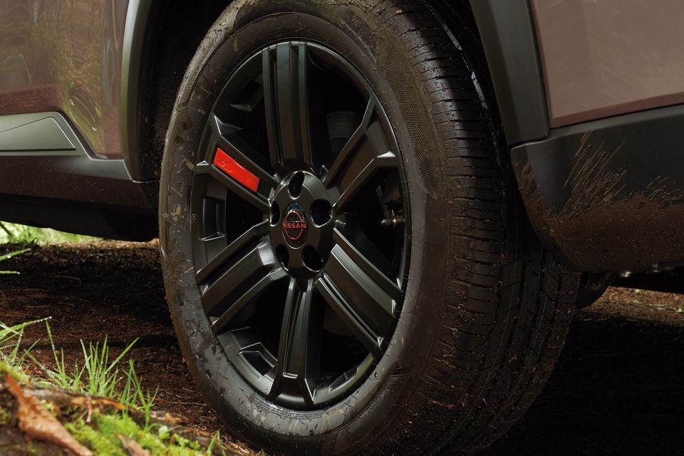 Close-up of a black alloy wheel and tyre on a Nissan X-Trail, with mud-splattered surroundings suggesting off-road use