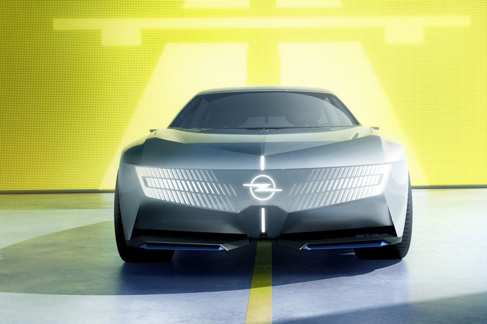 Carro-conceito Opel STX visto de frente, mostrando seu emblema de raio iluminado e barra de luz LED em frente a um fundo amarelo brilhante