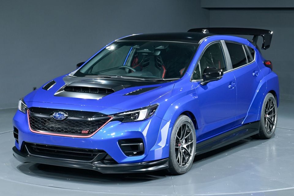 A blue Subaru WRX STI concept hatchback with large rear wing and hood scoop, displayed indoors at a motor show