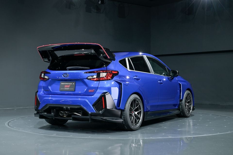 Rear three-quarter view of the blue Subaru Performance-B STI Concept hatchback on a motor show display turntable, featuring a large rear wing, STI badging, and aggressive body kit