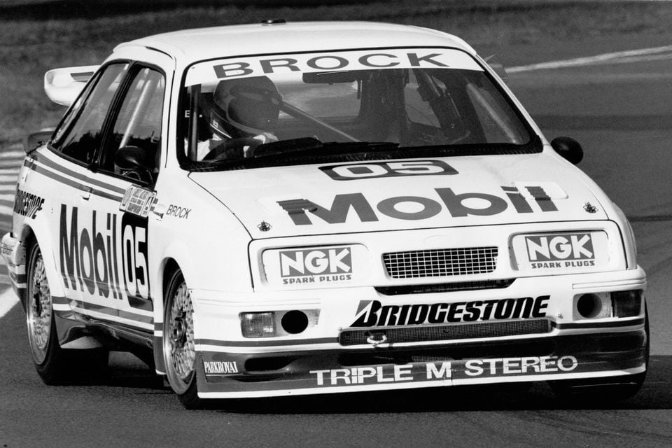 Peter Brock's Mobil-sponsored Ford Sierra race car number 05 on track at Sandown, seen from the front-side in a black and white photo