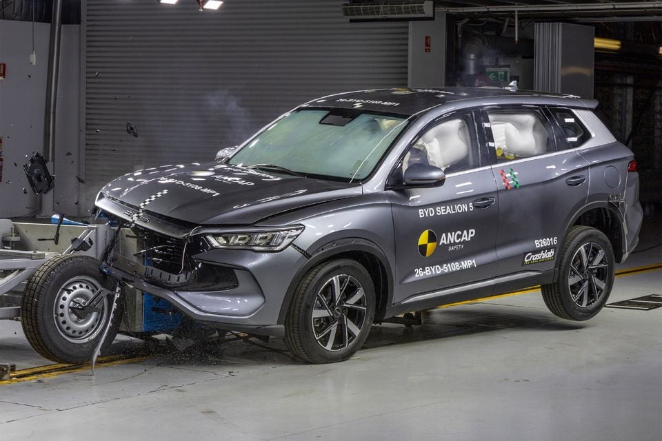 A grey BYD Sealion 5 SUV with deployed airbags sits damaged after a frontal offset crash test at an ANCAP safety testing facility.