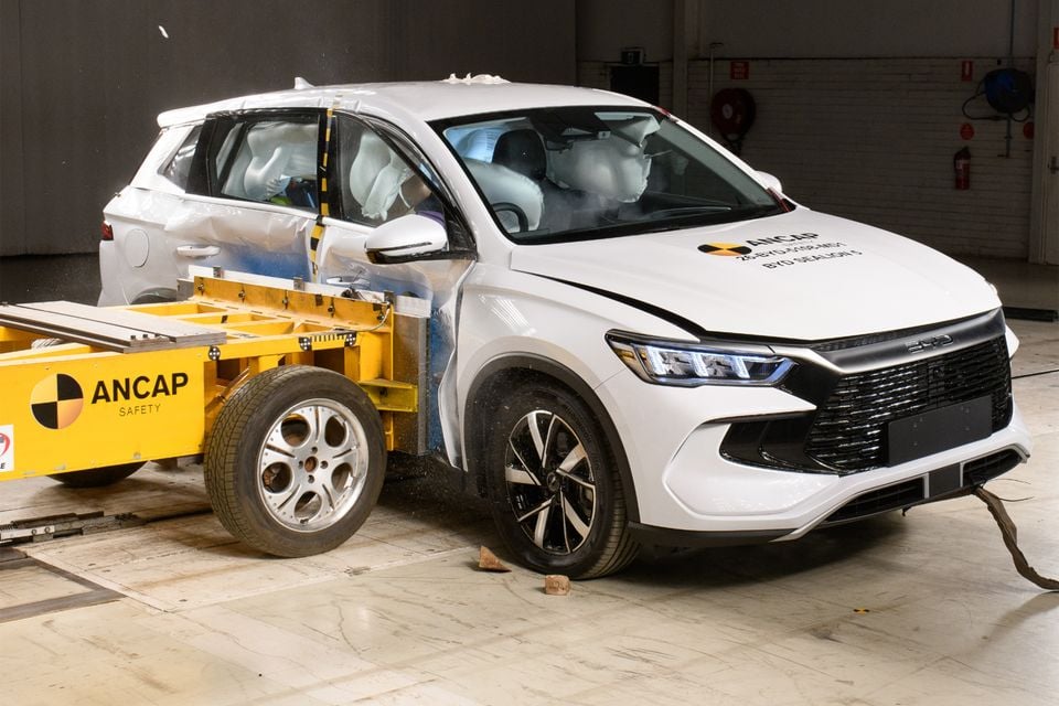 A white BYD Sealion 5 SUV with deployed airbags undergoes an ANCAP side-impact crash test in a testing facility.