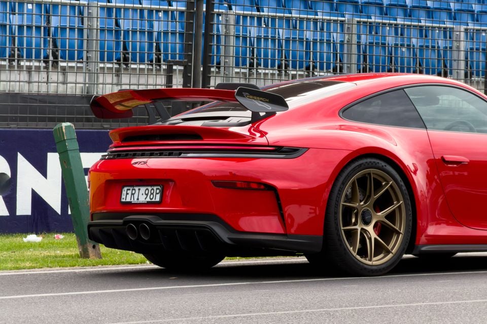 Rear and side view of a red Porsche 911 GT3 with Weissach package, featuring a large rear wing and gold alloy wheels, parked at a motorsport circuit