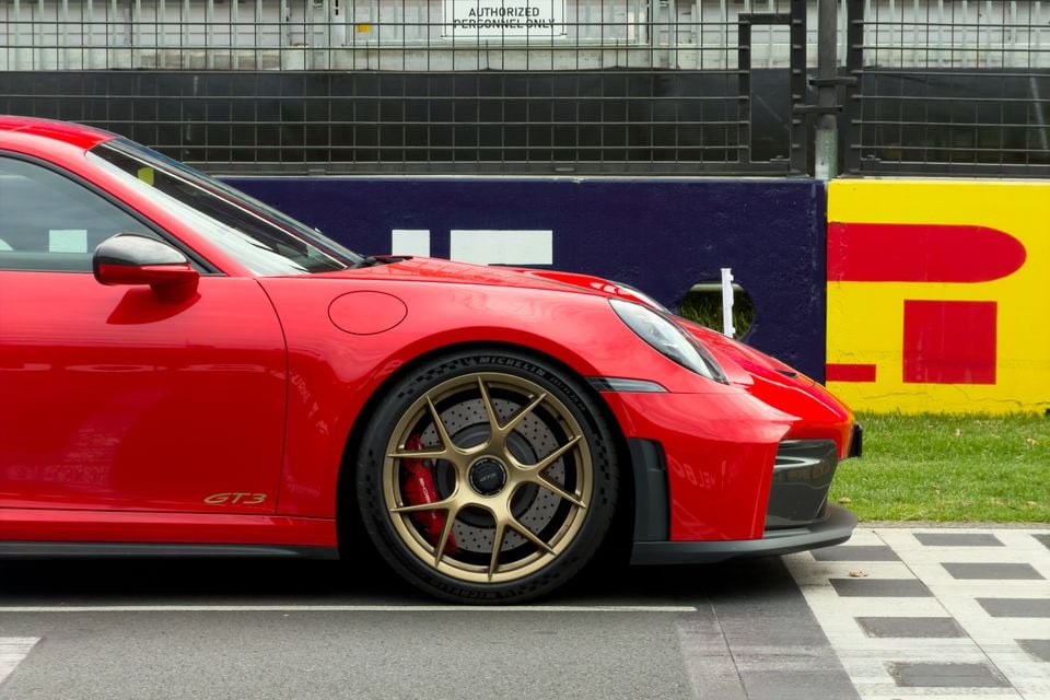 A red Porsche 911 GT3 with gold wheels and red brake calipers seen from the side at a motorsport circuit, with Pirelli barrier branding in the background