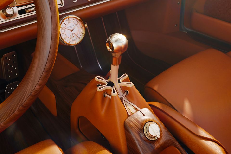 Luxury car interior showing a tan leather cabin with a gold gear shift knob, a Louis Vuitton clock on the dashboard, and a tan leather drawstring bag resting on the centre console, in a Porsche 911 reimagined by Singer and Louis Vuitton