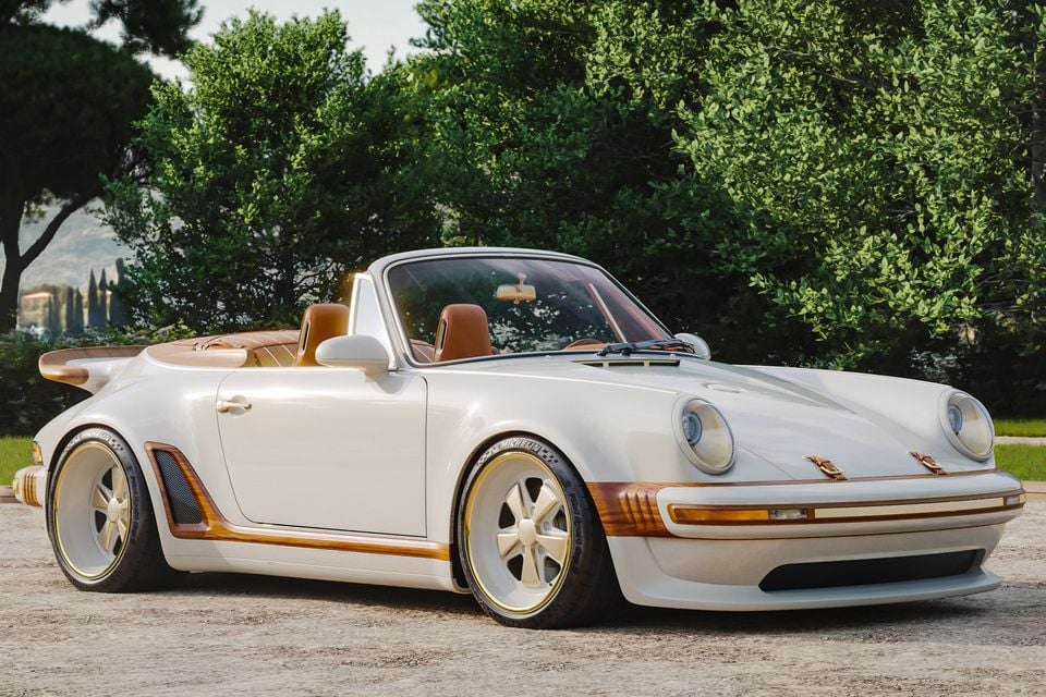 A white and gold custom Porsche 911 open-top sports car, reimagined by Singer and Louis Vuitton, seen from the front side with brown leather interior and wood trim accents