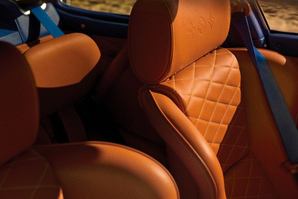 Tan leather interior of a Porsche 911 reimagined by Singer and Louis Vuitton, showing quilted diamond-stitched seats with embossed headrests and blue seatbelts