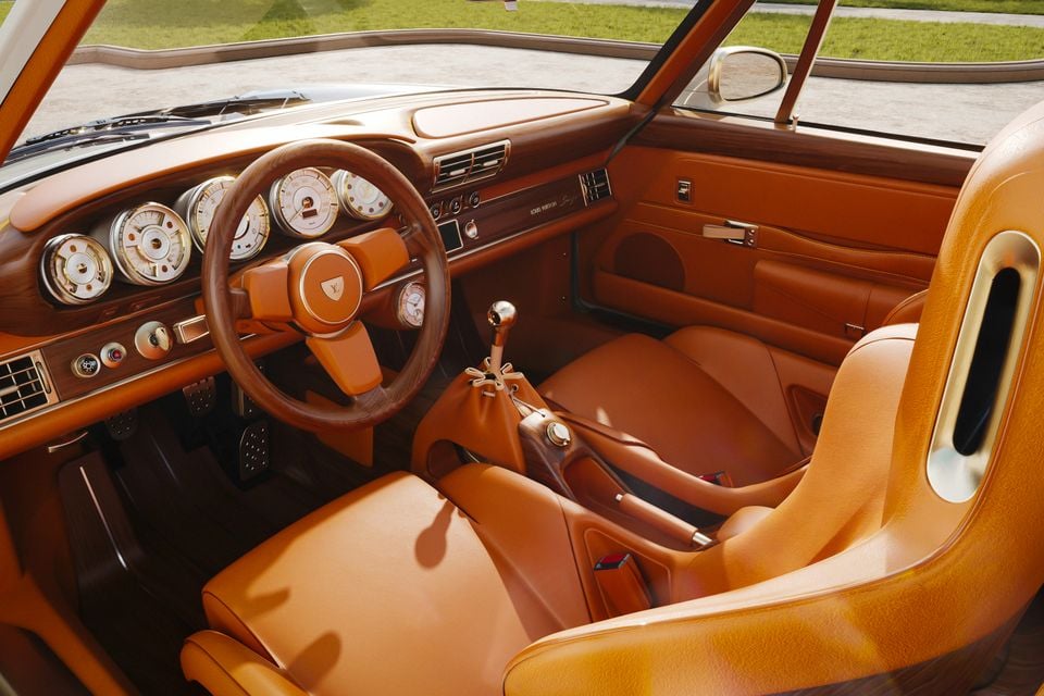 The tan leather interior of a Porsche 911 reimagined by Singer and Louis Vuitton, showing the wood-rimmed steering wheel, analogue gauges, manual gear shifter, and bucket seats