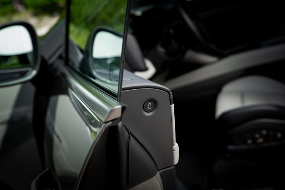 A close-up view of the automatic door handle button on a Porsche Cayenne Electric, with the seat and dashboard visible in the background.