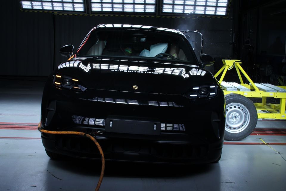 A black Porsche Cayenne Electric seen from the front during a Euro NCAP crash test, with a mobile deformable barrier visible to the right