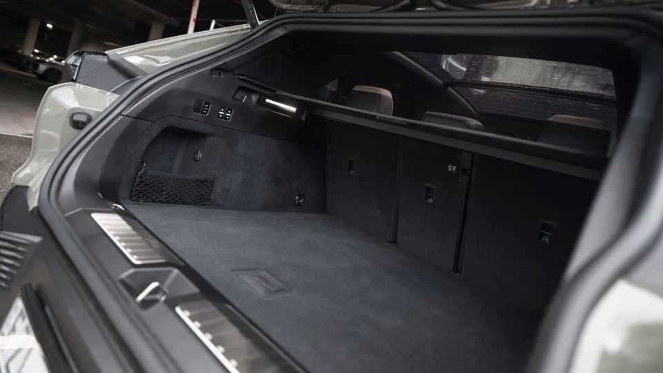 The open boot of a Porsche Cayenne S Electric, showing a spacious, carpet-lined cargo area with a cargo net and fold-flat rear seat controls, photographed in a car park.