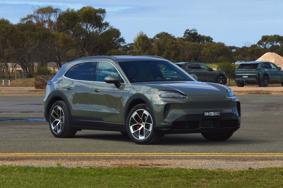 A green Porsche Cayenne S Electric SUV seen from the front-side on a paved road, with additional vehicles visible in the background against an Australian rural landscape.