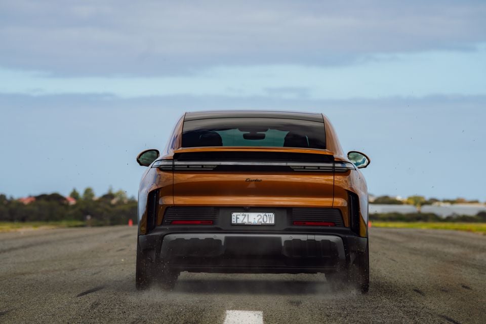 Rear view of an orange Porsche Cayenne Turbo Coupe electric SUV accelerating on a runway
