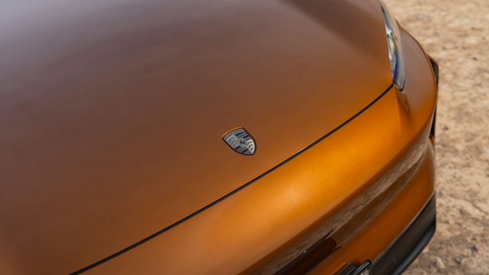 Close-up of the Porsche crest badge on the bonnet of an orange Porsche Cayenne Turbo Coupe Electric