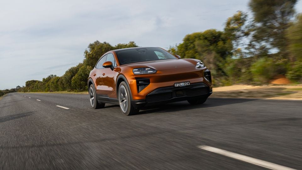 An orange Porsche Cayenne Turbo Electric Coupe SUV driving on a country road, seen from the front-side angle
